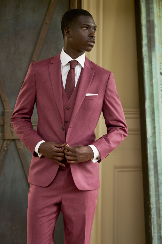 Man wearing a pink suit with a white shirt and red tie indoors.